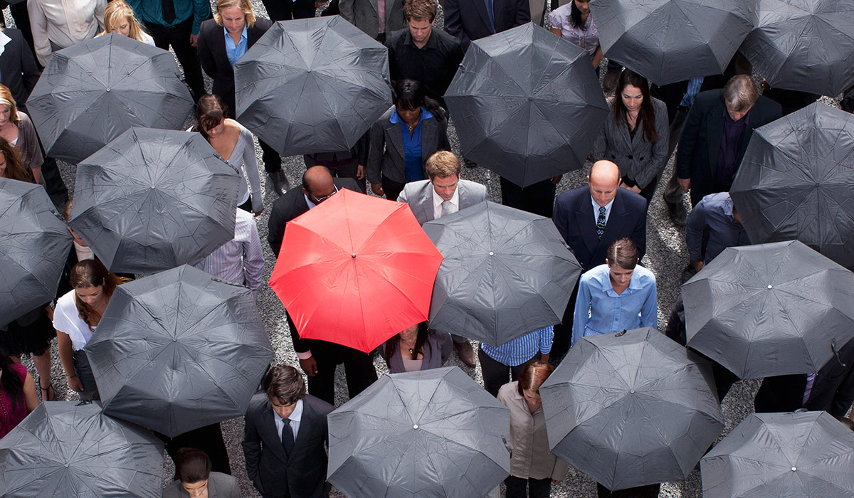 A red umbrella standing out in crowd of business people. Image credit: iStock