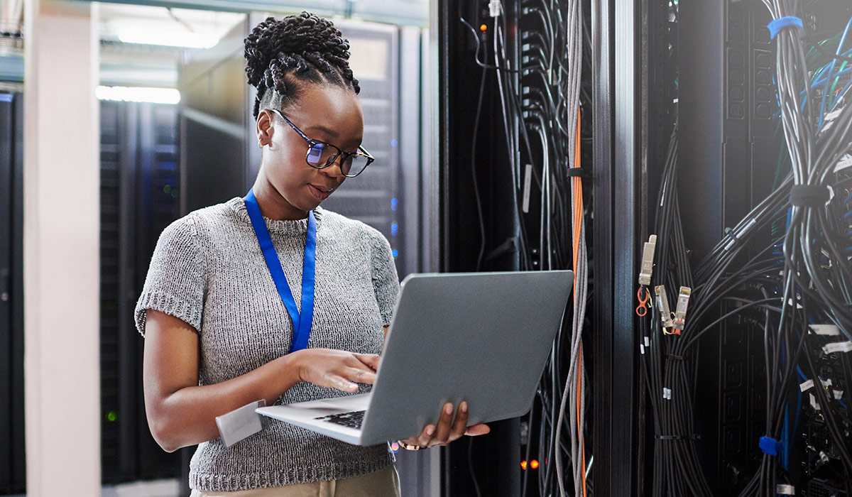 A young woman using a laptop in a server room. Image credit: iStock